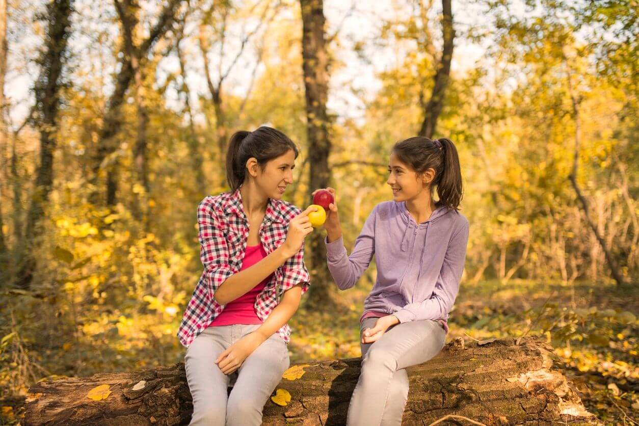 Two girls holding apples in a forest.