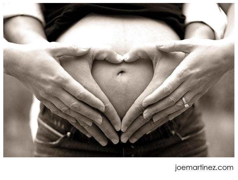 Hands forming heart on pregnant belly.