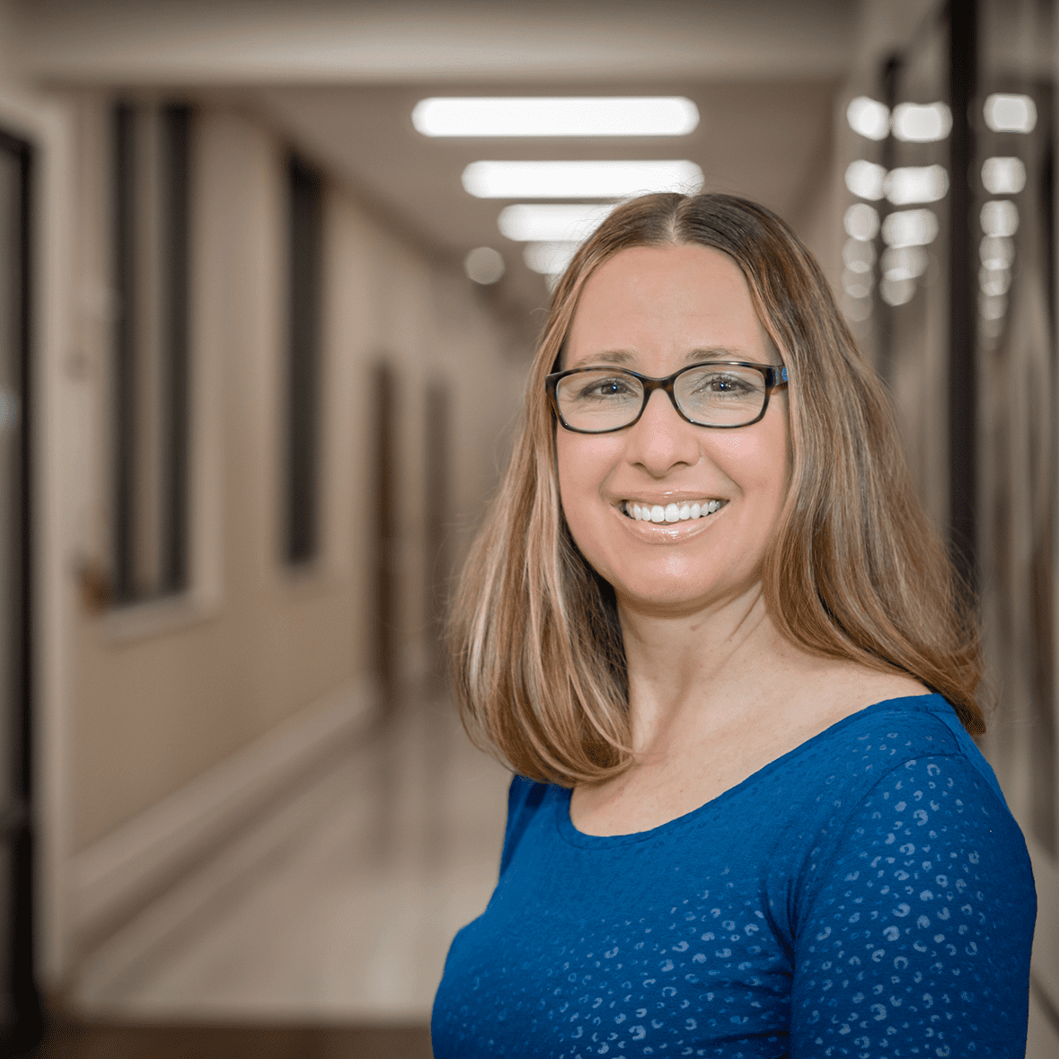 Smiling woman in blue shirt, wearing glasses.